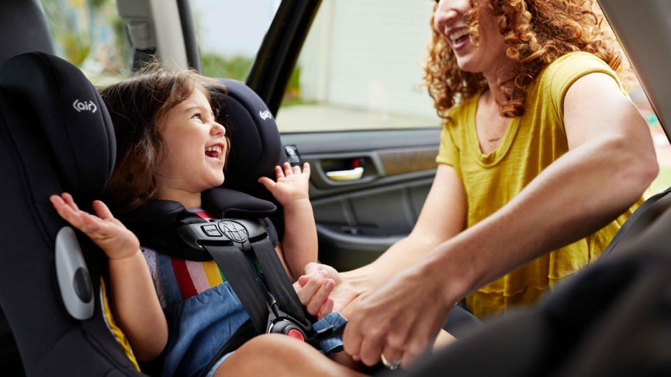 Little girl smiling while mother buckles her into her car seat