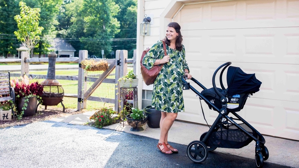woman in green dress pushing a stroller with an infant car seat attached