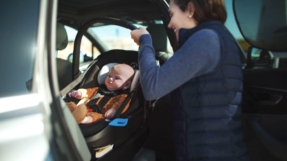 infant in an orange onesie being buckled into an infant car seat