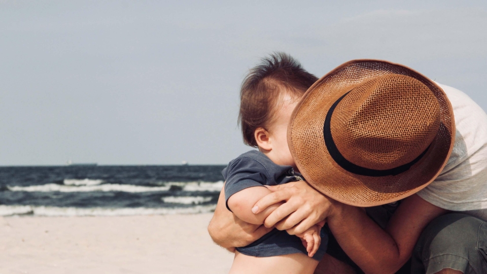 Man wearing a hat hugging baby on beach