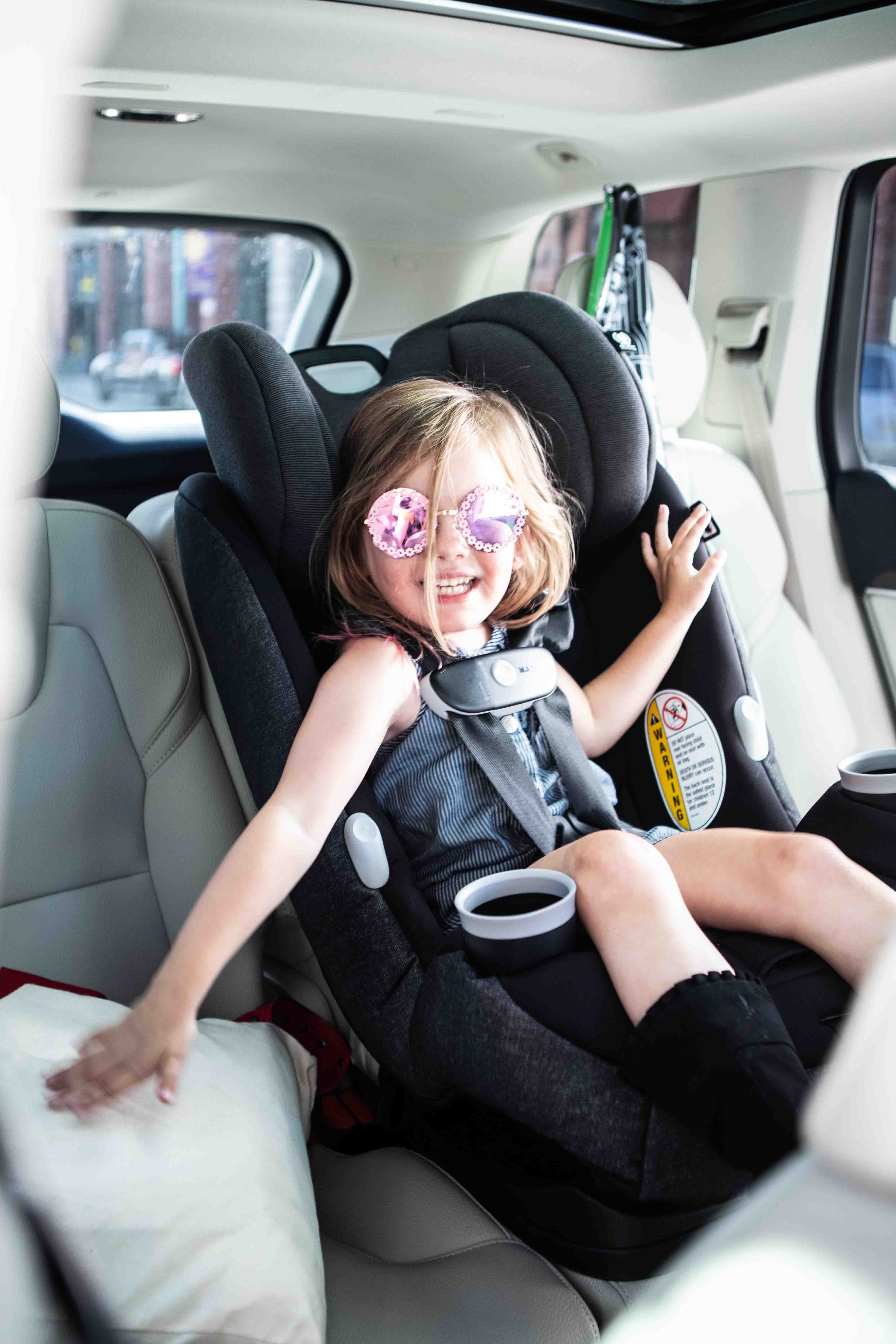 Little girl wearing sunglasses smiling in convertible car seat